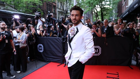 Jonathan Bailey im weißen Anzug mit großer Kunstblume am Revers bei der Met Gala 2024