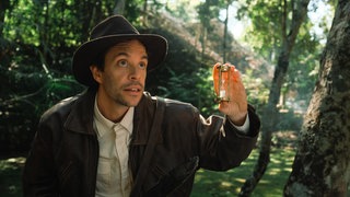 Tobias Krell als Checker Tobi zwischen Bäumen, in der Hand hält er eine Sanduhr