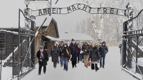 Zu sehen ist eine Schulklasse unter dem Eingangstor des Konzentrationslagers in Auschwitz. KZ-Besuche und Gespräche mit Zeitzeugen können eine große Bedeutung haben.