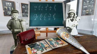 Brottasche, Fibel und Zuckertüte liegen auf einer historischen Schulbank im Museum Viadrina in der Sonderausstellung "Von ABC Schützen und Zuckertüten": Schulen gab es bereits bei den Sumerern, also im 3. bis 4. Jahrtausend vor Christus. 