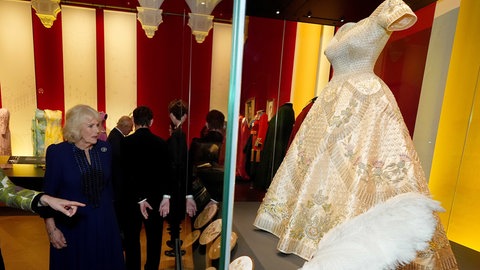 Königin Camilla betrachtet das Krönungskleid von Elizabeth II. in einer Londoner Ausstellung.