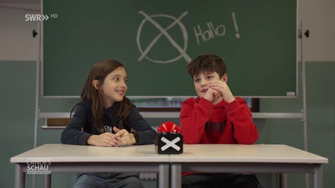 zwei kinder sitzen an der Schulbank vor einer tafel