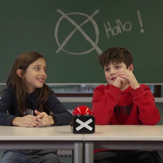 zwei kinder sitzen an der Schulbank vor einer tafel