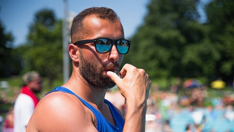 Bademeister im Muskelschirt mit verspiegelter Sonnebrille und Trillerpfeife im Freibad