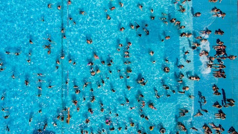 Luftbild von einem Schwimmbecken im Freien, in dem sich viele Menschen tummeln