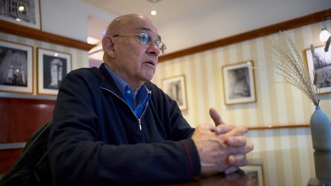 Historiker Tom Segev im Gespräch. Mit gefalteten Händen sitzt er in einem Wiener Kaffeehaus. (2023)