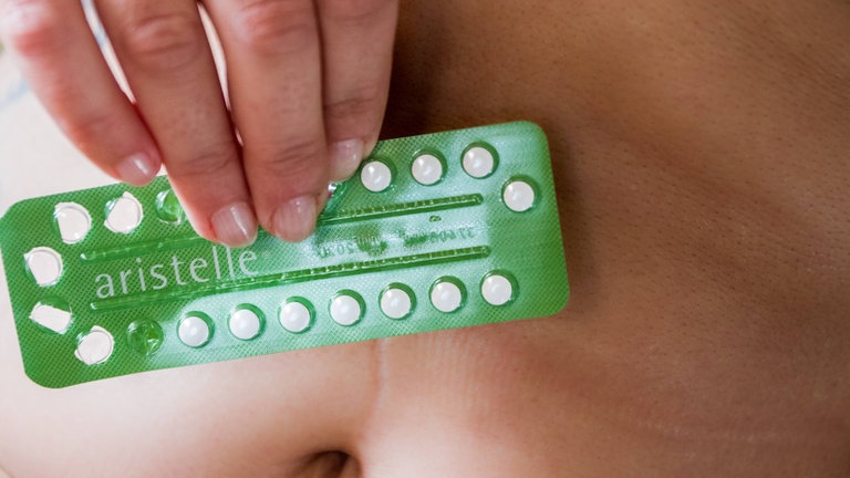 Frau hält eine angebrochene Packung der Pille aristelle zur Schwangerschaftsverhütung vor den Bauch 