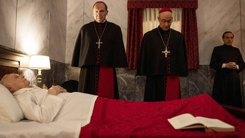 Ralph Fiennes als Camerlengo und Stanley Tucci als Papabile Aldo Bellini am Totenbett des verstorbenen Papstes, im Film „Konklave“ von Edward Berger. 