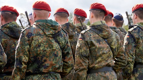 Eine Gruppe von Soldaten der Deutschen Bundeswehr in Tarnuniformen stehen in Formation mit Gewehr bei einem Appell.