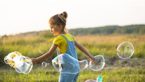 Ein Mädchen macht Seifenblasen auf einer Wiese 
