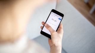 Eine Frau hält ein iPhone in der Hand und benutzt die Internet-Suchmaschine Google.