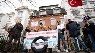 In Hamburg lebende Journalistinnen und Journalisten aus der Türkei stehen mit einem schwarzen Kranz vor dem Türkischen Konsulat.