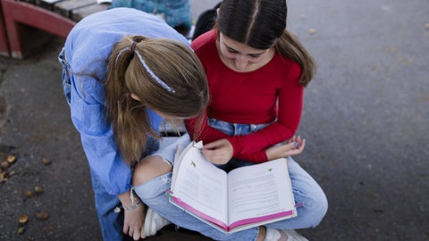 Zwei Schülerinnen auf dem Schulhof schauen in Buch.