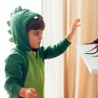 Kind im Dinokostüm spielt mit Dinosauriern