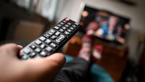 Ein junger Mann sitzt mit einer Fernbedienung vor dem Fernseher