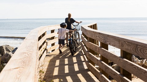 Zwei Geschwister laufen über eine Brücke ans Meer