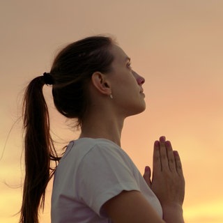 Junge Frau betet bei Sonnenuntergang