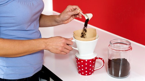 Eine Frau befuellt einen Kaffeefilter mit Kaffeepulver