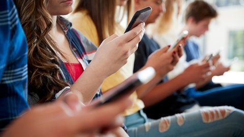 Mehrere Jugendliche sitzen am Handy