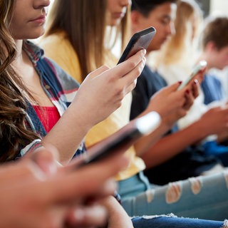 Mehrere Jugendliche sitzen am Handy