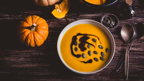 Eine Schale Kürbissuppe mit Kürbiskernöl und Kürbiskernen, umgeben von Kürbissen.