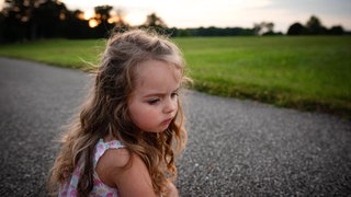 Kleines Mädchen sitzt nachdenklich im Freien