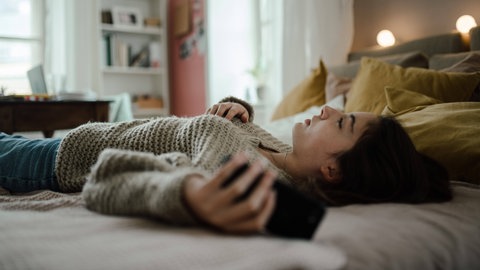 Frau liegt mit Smartphone in der Hand auf dem Bett