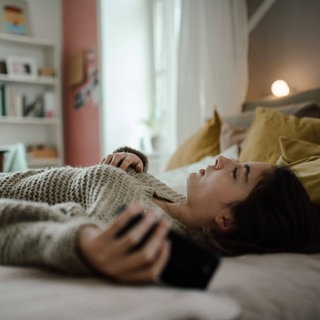 Frau liegt mit Smartphone in der Hand auf dem Bett
