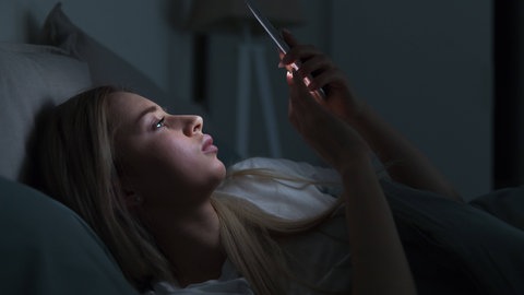 Frau liegt auf dem Bett und schaut in ihr Handy