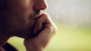 Junger Mann in Nahaufnahme stützt sein Kinn auf die Hand