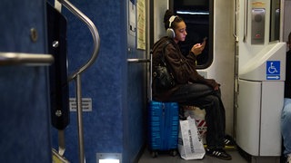 Frau sitzt auf einem Koffer im Zug und trägt Kopfhörer