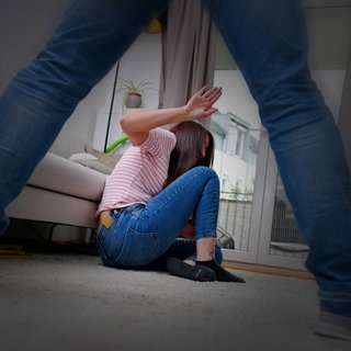 Symbolfoto: Ein Mann bedroht eine junge Frau in der gemeinsamen Wohnung, sie nimmt eine Abwehrhaltung ein, um sich gegen die drohenden Schläge zu schützen.