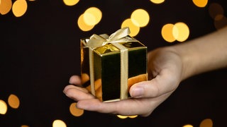 Eine Hand hält eine goldene Geschenkbox mit goldenem Band.