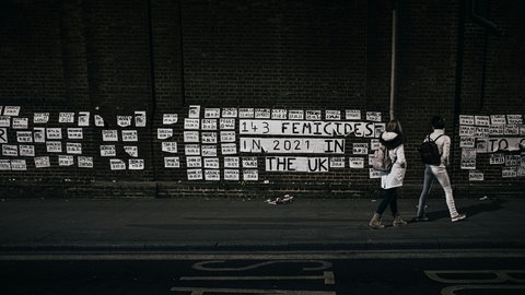 Mahnposter an Häuserwand an dem ein Paar vorübergeht