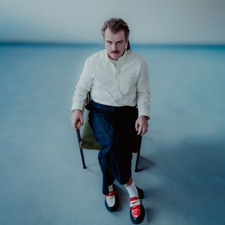 Artur Weigandt sitzt auf einem Stuhl mitten in einem Raum