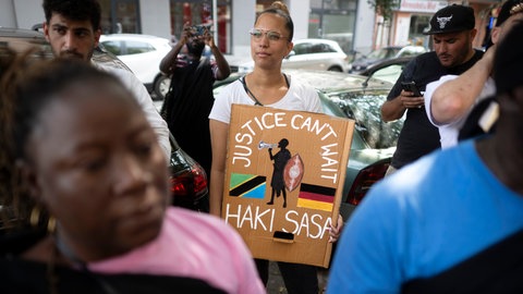 Demonstrantin mit Plakat "Justice Can't Wait Haki Sasa" beim Gedenkmarsch und der Zeremonie zur Straßenumbenennung der Petersallee in die Maji-Maji-Allee im Afrikanischen Viertel in Berlin (2024)