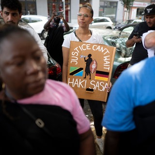 Demonstrantin mit Plakat "Justice Can't Wait Haki Sasa" beim Gedenkmarsch und der Zeremonie zur Straßenumbenennung der Petersallee in die Maji-Maji-Allee im Afrikanischen Viertel in Berlin (2024)
