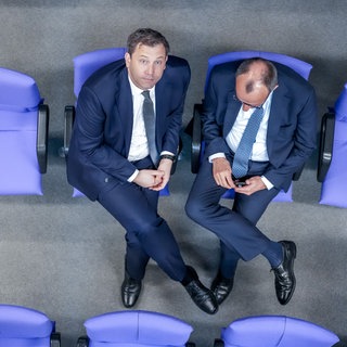 Bundesfinanzminister Lars Klingbeil und Bundeskanzler Friedrich Merz während einer Debatte auf den hinteren Rängen des Bundestages