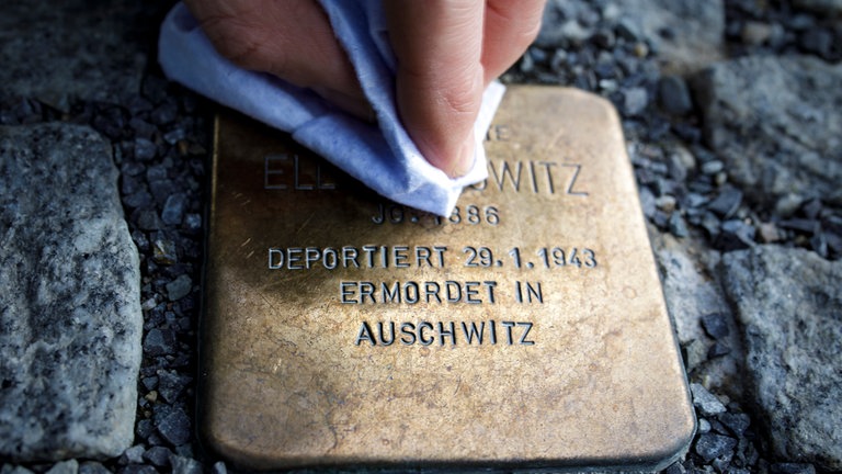 Eine Person putzt einen Stolperstein, der an die Verfolgte des Nationalsozialismus und in Auschwitz ermordete Ella Horowitz erinnert. 