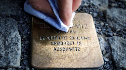 Eine Person putzt einen Stolperstein, der an die Verfolgte des Nationalsozialismus und in Auschwitz ermordete Ella Horowitz erinnert. 