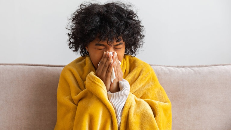 Unglückliche, erkrankte junge Frau mit Erkältung sitzt zu Hause auf dem Sofa.