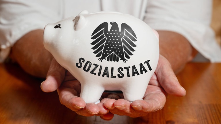 Ein weißes Sparschwein mit der Aufschrift Sozialstaat symbolisiert die staatliche Verantwortung für Absicherung, Umverteilung und die Finanzierung sozialer Leistungen in Deutschland.