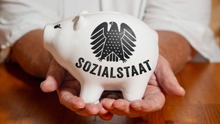 Ein weißes Sparschwein mit der Aufschrift Sozialstaat symbolisiert die staatliche Verantwortung für Absicherung, Umverteilung und die Finanzierung sozialer Leistungen in Deutschland.