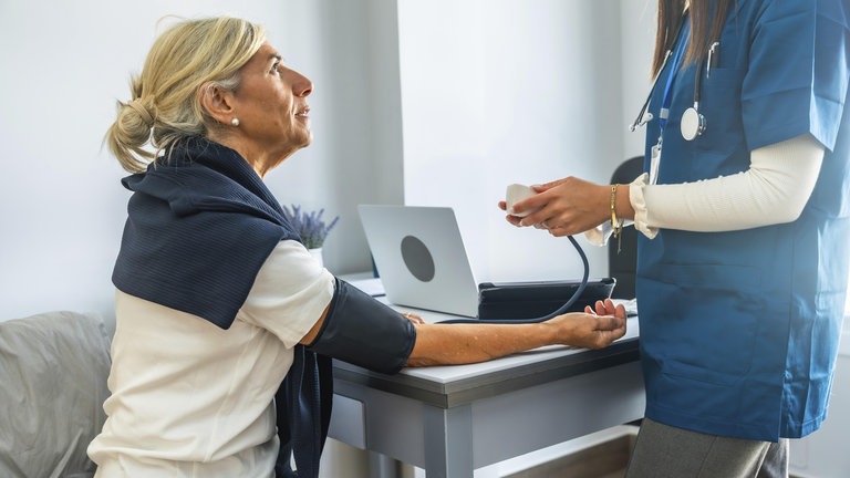 Ärztliches Fachpersonal überwacht und zeichnet den Blutdruck eines älteren Patienten mit einem Blutdruckmessgerät während einer regelmäßigen Gesundheitsuntersuchung auf, wobei der Schwerpunkt auf der Gesundheitsvorsorge liegt