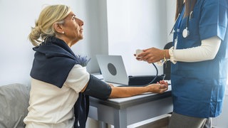 Ärztliches Fachpersonal überwacht und zeichnet den Blutdruck eines älteren Patienten mit einem Blutdruckmessgerät während einer regelmäßigen Gesundheitsuntersuchung auf, wobei der Schwerpunkt auf der Gesundheitsvorsorge liegt