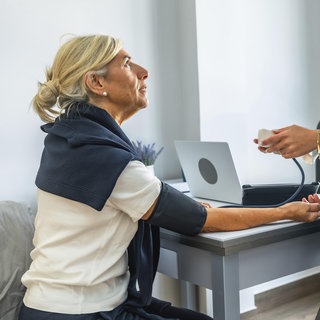 Ärztliches Fachpersonal überwacht und zeichnet den Blutdruck eines älteren Patienten mit einem Blutdruckmessgerät während einer regelmäßigen Gesundheitsuntersuchung auf, wobei der Schwerpunkt auf der Gesundheitsvorsorge liegt