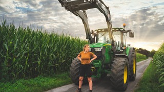 Landwirtin steht entschlossen vor einem Traktor