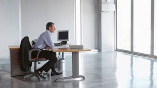 Mann sitzt an einem Schreibtisch in einem leeren Büro und genießt die Einsamkeit. Symbolfoto.