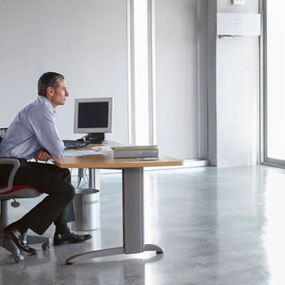 Mann sitzt an einem Schreibtisch in einem leeren Büro und genießt die Einsamkeit. Symbolfoto.