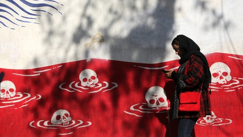 Frau geht in Teheran an einer Hauswand mit antiamerikanischen Wandgemälden vorbei.